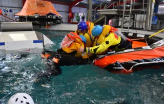 OPITO BOSIET Course in the stream marine training pool, men in hi-vis life jackets assist an individual out of the pool into a safety raft