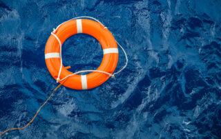 Bright orange lifebuoy floating on deep blue sea, symbolising maritime safety and security awareness at sea.