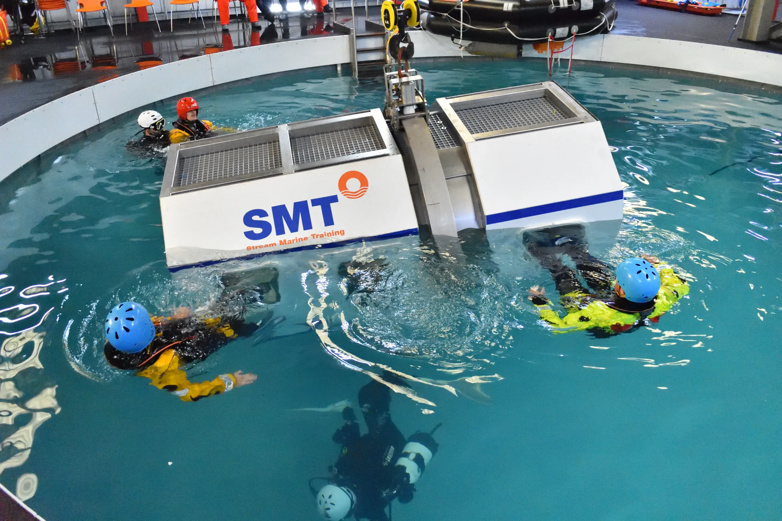 HUET Simulator in water with delegates escaping via the windows with the aid of the stream marine training diver team.
