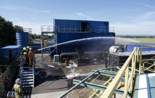 Firefighting trainees at Stream Marine Training in Glasgow practising hose techniques during live fire safety drills on the outdoor fire ground.