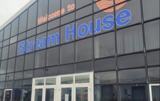 A tall glass structure with the words and logo Stream House in the stream marine training orange and blue colours.