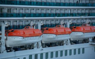 Row of orange and white lifeboats secured on the side of a cruise ship, ready for launch as part of PST safety training drills.