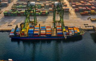 Aerial view of a busy shipping port with cranes loading colourful cargo containers onto a vessel, representing global maritime regulation and training standards.