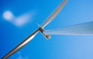 A close up view looking up at a wind turbine rotor and blades set against a bright blue sky, representing the growing demand for skilled workers in the UK wind energy sector and GWO training pathways.