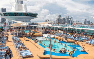 Busy sun deck and pool area on a large cruise ship with passengers relaxing and swimming, showing the scale of modern cruise vessels often staffed by crew with STCW training.